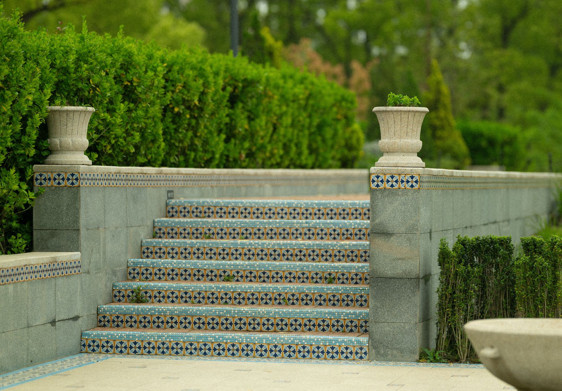 Patterned tiled garden steps between stone walls and clipped hedges