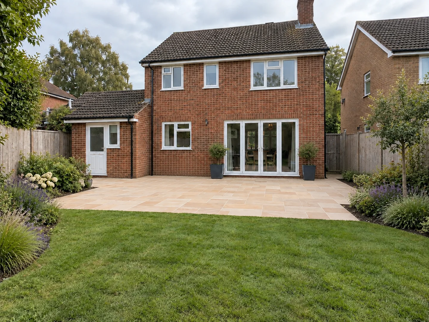Pale stone patio connecting the rear of a brick house to the lawn